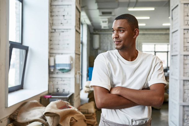 Young caucasian black worker or business owner on coffee factory or warehouse. Coffee process making, production and storage. Small business. Man with crossed arms looking away - 写真・画像