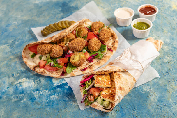 Traditional Mediterranean Arabic grilled halloumi and falafel, hummus and vegetables in flatbread wraps with herbs and a variety of sauces - 写真・画像