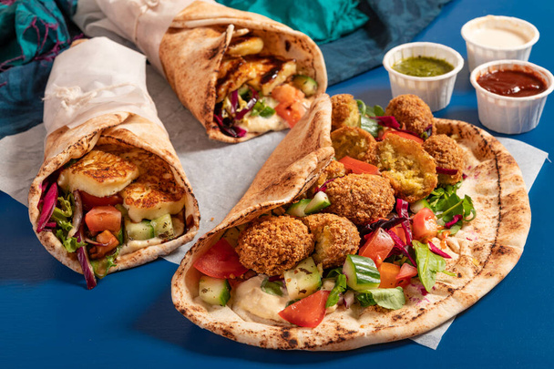 Tradicional mediterráneo árabe a la parrilla halloumi y falafel, hummus y verduras en envolturas de pan plano con hierbas y una variedad de salsas - Foto, imagen