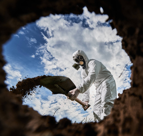 Widok z wnętrza dziury nierozpoznawalnego męskiego naukowca w masce gazowej przy użyciu łopaty do kopania gleby w strefie zagrożenia, analiza środowiska przyrodniczego, profesjonalny ekolog badający zanieczyszczenia. - Zdjęcie, obraz