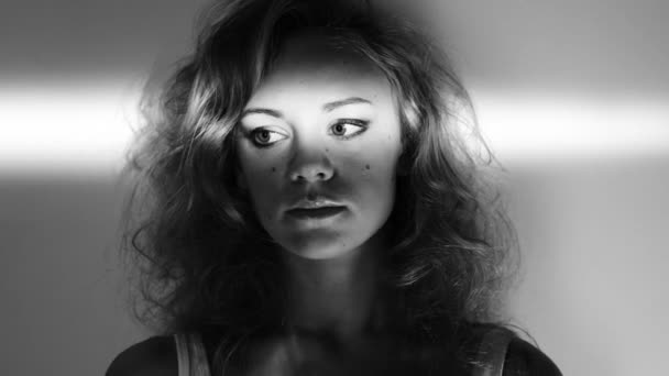 Czarno-białe nagranie wideo 4k pięknej młodej kobiety stojącej pod ścianą ze światłem świecącym nad oczami. - Materiał filmowy, wideo