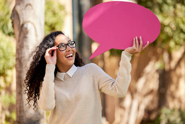 Fotografía de una hermosa joven estudiante sosteniendo una burbuja del habla sobre su cabeza mientras estaba de pie afuera. - Foto, imagen
