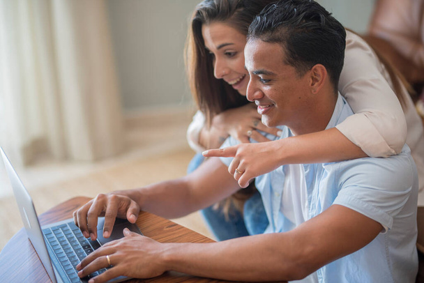 Міжрасові пари розважаються разом вдома, використовуючи ноутбук та інтернет. Концепція молодих людей, що живуть разом з любов'ю і стосунками дозвілля. Новий одружений хлопчик і дівчинка посміхаються
 - Фото, зображення
