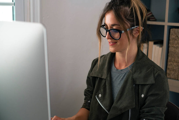 Genç iş kadını girişimci ofisteki bilgisayarlarda çalışıyor, gülümsüyor ve özgürlüğün tadını çıkarıyor. Çevrimiçi iş yapan modern kadınlar. Bilgisayarda akıllı çalışma üzerine yazan güzel kişi - Fotoğraf, Görsel