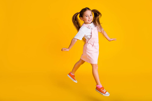 Photo of pretty cute school girl wear summer overall jumping high empty space isolated yellow color background. - Zdjęcie, obraz