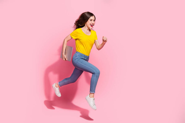 Full size photo of cute young brunette lady run with laptop wear t-shirt jeans shoes isolated on pink background. - Zdjęcie, obraz
