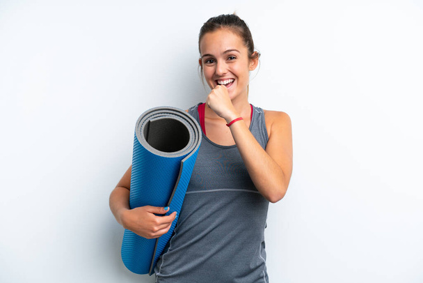 Young sport woman going to yoga classes while holding a mat isolated on white background celebrating a victory - Фото, изображение