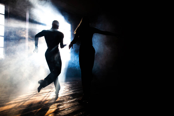 Un par de bailarines de salón profesionales bailan en el estudio loft. Hermosa actuación artística con humo pesado. Concepto de vida deportiva. Pasión y danza emocional. - Foto, imagen