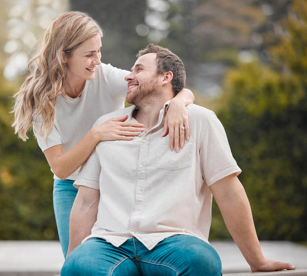 Happy young caucasian couple bonding together during a day outdoors in the garden. Beautiful smiling woman holding and embracing her handsome husband. Showing love and affection and gazing lovingly. - Foto, afbeelding