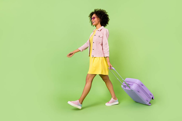 Full length πορτρέτο προφίλ της όμορφης χιλιετηρίδας κορίτσι κρατήσει τσάντα με τα πόδια εγγραφή απομονώνονται σε πράσινο φόντο χρώμα. - Φωτογραφία, εικόνα