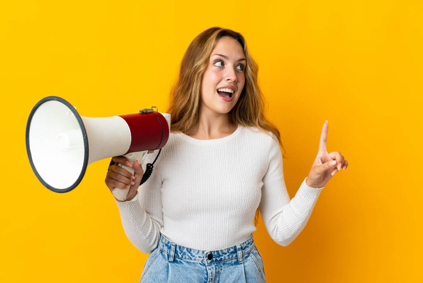 Young blonde woman isolated on yellow background holding a megaphone and intending to realizes the solution - Φωτογραφία, εικόνα