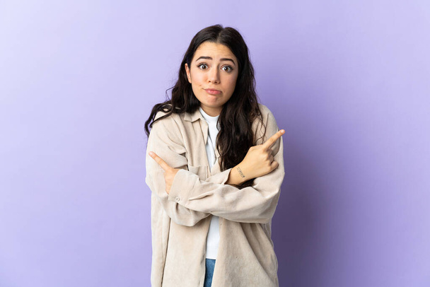 Young caucasian woman isolated on purple background pointing to the laterals having doubts - Photo, Image