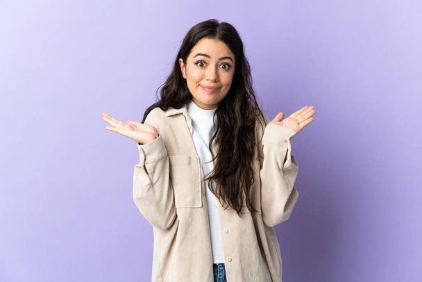 Young caucasian woman isolated on purple background making doubts gesture - Фото, зображення
