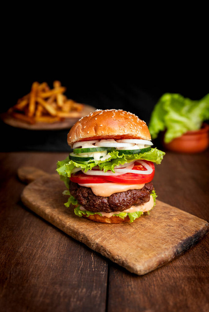 Burger with beef meat, cheese, lettuce, onion, tomato, cucumber, mayo and ketchup on an old wooden table. Junk and unhealthy food concept - Photo, image