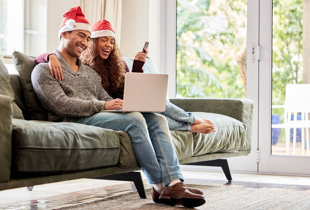 Zdjęcie młodej pary robiącej zakupy online w kapeluszach świątecznych w domu. - Zdjęcie, obraz