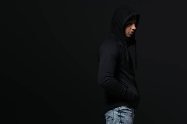 Side view of african american hooligan in hoodie standing isolated on black  - Фото, изображение