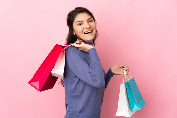 Teenager rusky dívka izolované na růžovém pozadí drží nákupní tašky a usmívá - Fotografie, Obrázek