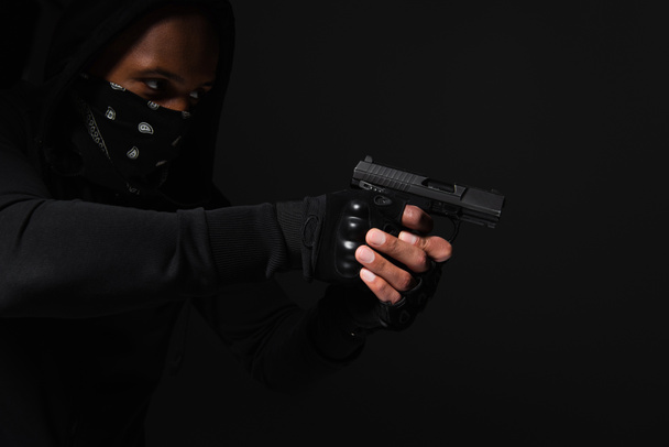African american bandit with obscure face holding handgun isolated on black  - Photo, Image