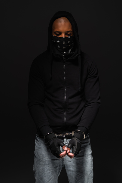 African american bandit with mask on face and handcuffs standing isolated on black  - Foto, Imagem