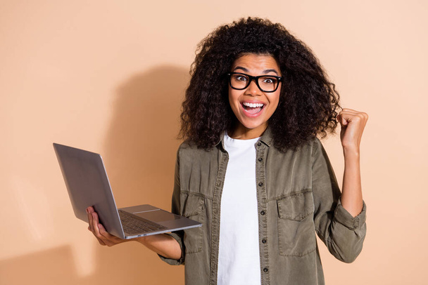Photo of young african lady rejoice success triumph achievement fist hand hold laptop isolated over beige color background. - 写真・画像