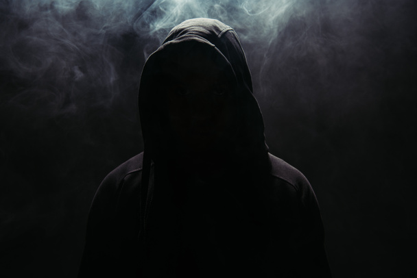Silhouette of hooligan in hood on black background with smoke  - Foto, Imagen