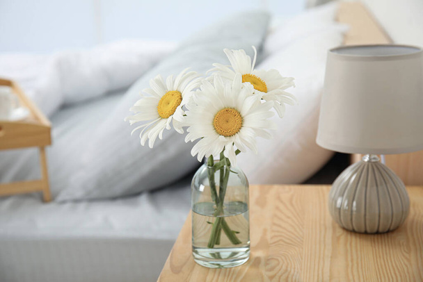Bouquet of beautiful daisy flowers and lamp on nightstand in bedroom - Photo, Image