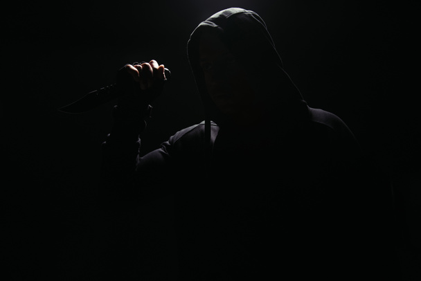 Silhouette of bandit in hoodie holding knife isolated on black  - Foto, immagini