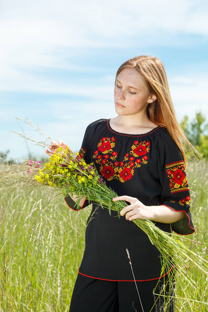 Piękna dziewczyna w czarnej vyshyvanka z kwiatami na polu z widokiem na niebo zbliżenie - Zdjęcie, obraz