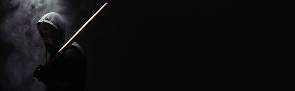 Vista lateral de silueta de hooligan afroamericano con bate de béisbol sobre fondo negro con humo, pancarta   - Foto, Imagen