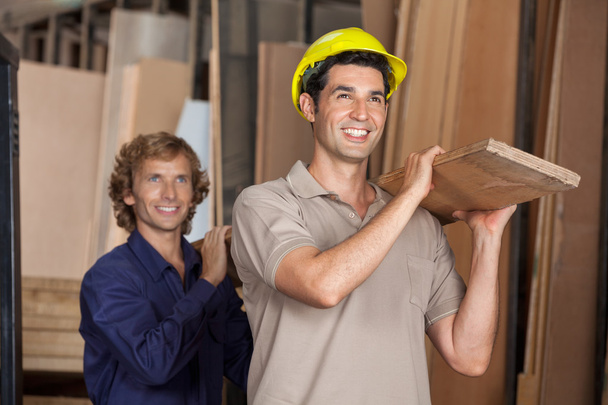 Carpenters Carrying Plank While Looking Away - Photo, Image