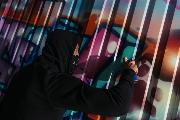 Вид сбоку на африканских вандалов, рисующих граффити на стене ночью  - Фото, изображение