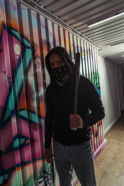 African american vandal holding baseball bat near graffiti on wall  - 写真・画像