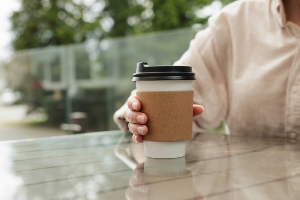 Woman holding paper takeaway cup at glass table outdoors, closeup. Coffee to go - Foto, immagini
