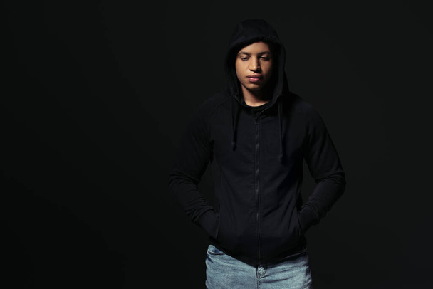 African american hooligan holding hands in pockets of hoodie isolated on black - Foto, Imagen
