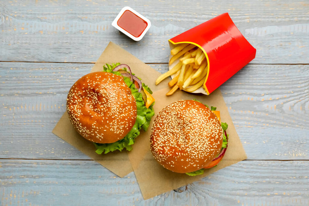Frietjes, hamburgers en ketchup op grijze houten tafel, plat gelegd. Fast food - Foto, afbeelding
