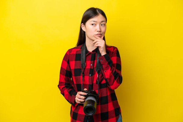 Nuori valokuvaaja Kiinalainen nainen eristetty keltaisella pohjalla, jolla on epäilyksiä ja sekava ilme - Valokuva, kuva