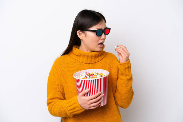 Young Chinese woman isolated on white background with 3d glasses and holding a big bucket of popcorns while looking side - Photo, Image