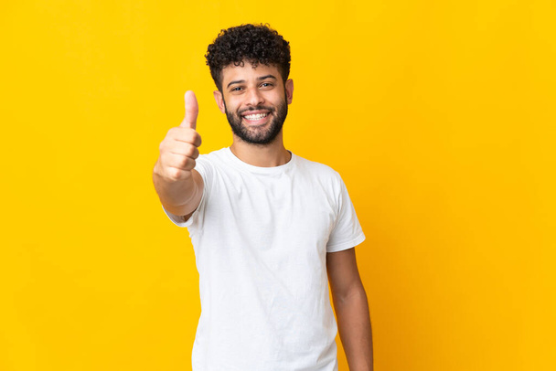 Young Moroccan man isolated on yellow background with thumbs up because something good has happened - Fotó, kép