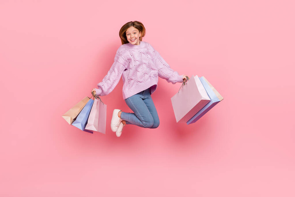 Photo of adorable cute girl knitwear sweater holding shopping bags jumping high isolated pink color background. - Foto, Imagem