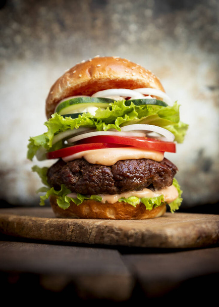 Burger with beef meat, cheese, lettuce, onion, tomato, cucumber, mayo and ketchup on an old wooden table. Junk and unhealthy food concept - Photo, image