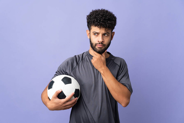 Guapo marroquí joven futbolista hombre sobre aislado en púrpura fondo teniendo dudas y pensando - Foto, imagen