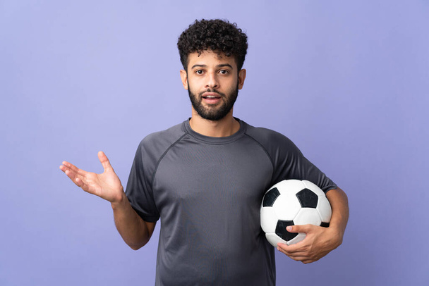 Schöner junger marokkanischer Fußballspieler mit schockiertem Gesichtsausdruck auf violettem Hintergrund - Foto, Bild