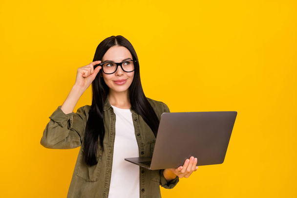 Photo of pretty young lady hold laptop look ad wear eyewear khaki shirt isolated on yellow background. - Zdjęcie, obraz