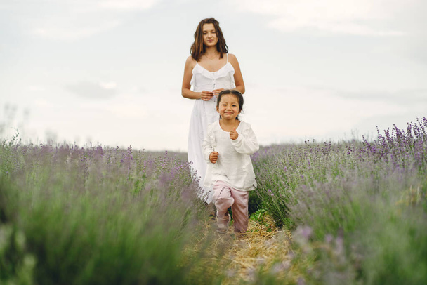 Mother with little daughter on lavender background. Beautiful woman and cute baby playing in meadow field. Family holiday in summer day. - Foto, immagini