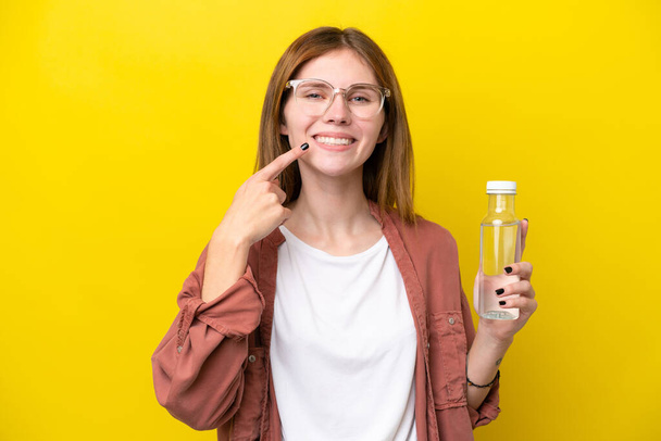 Молодая английская женщина с бутылкой воды, изолированной на желтом фоне, показывая большой палец вверх. - Фото, изображение