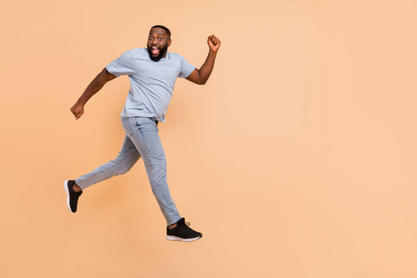Full length body size view of attractive cheerful sportive guy jumping having fun running isolated over beige pastel color background. - Фото, изображение