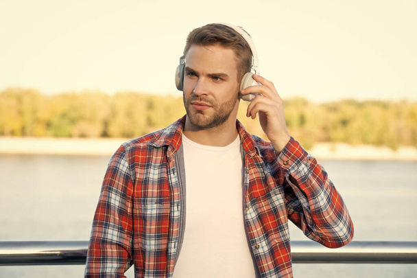 handsome unshaven man in checkered shirt listen music in headphones outdoor, modern life. - Foto, Bild
