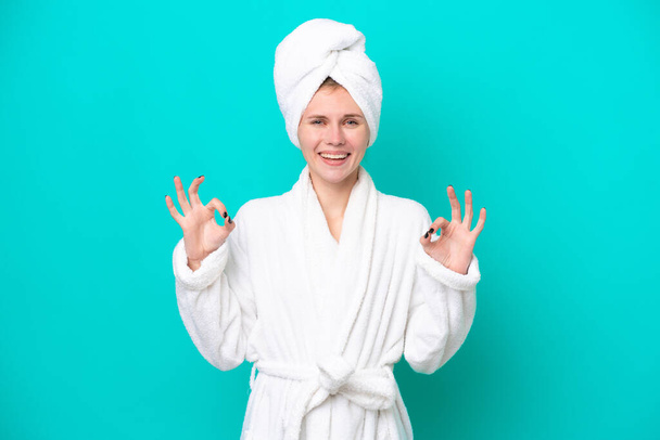 Young woman in a bathrobe isolated on blue background showing an ok sign with fingers - Foto, Bild