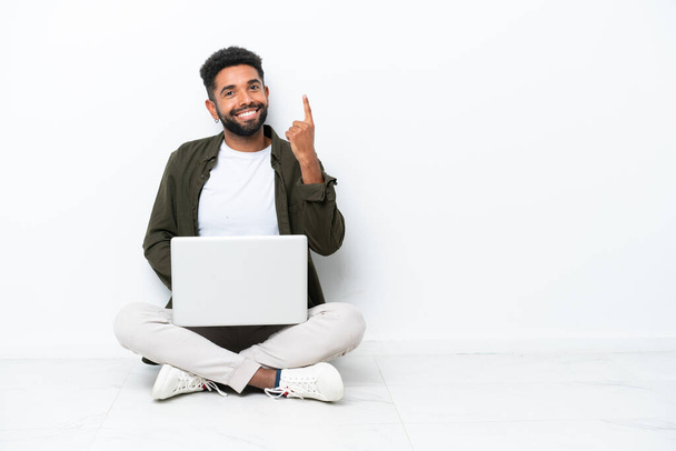 Young Brazilian man with a laptop sitting on the floor isolated on white pointing with the index finger a great idea - Foto, immagini
