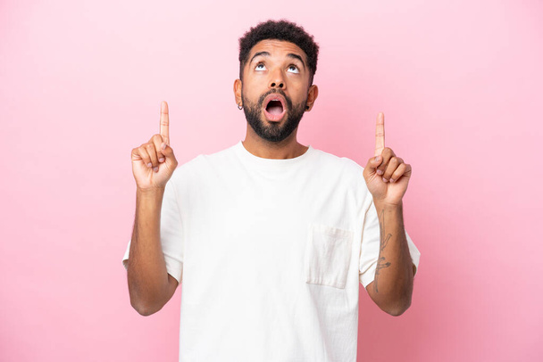 Young Brazilian man isolated on pink background surprised and pointing up - 写真・画像
